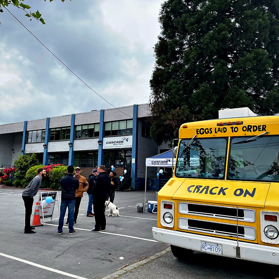 Customers chatting in the parking lot outside the Cascade Aqua-Tech Burnaby branch next to a yellow food truck, with blue balloons at the entrance