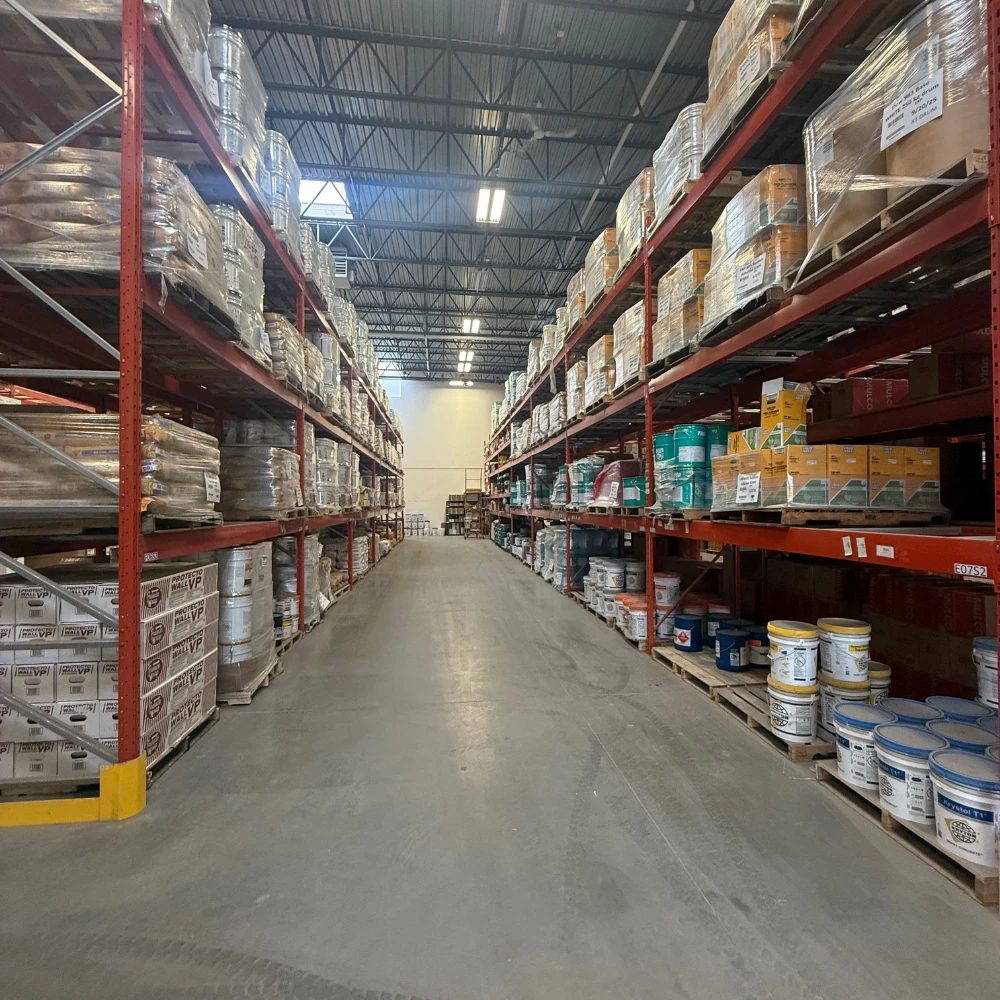 A fully stocked Cascade Aqua-Tech warehouse aisle with pallets of sealants, membranes and coatings on red racking